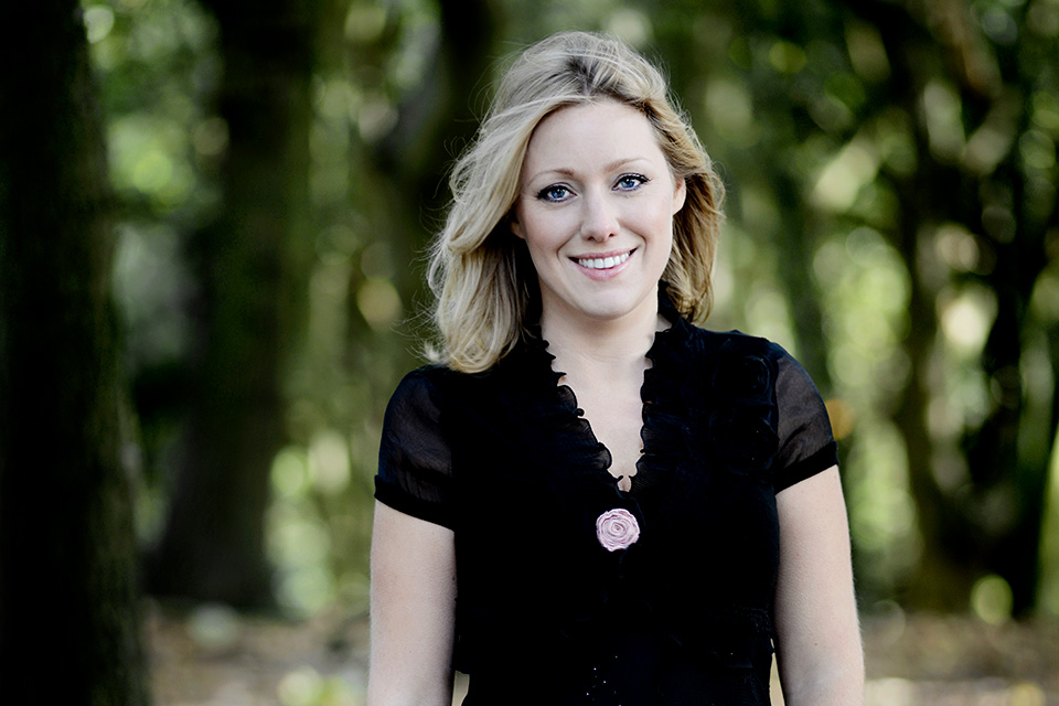 A blonde woman dressed in black looking into the camera 